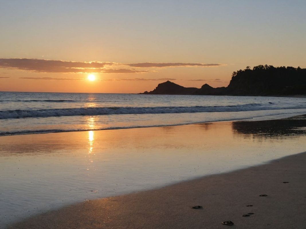 Beach at sunset with sandals and distant woman.