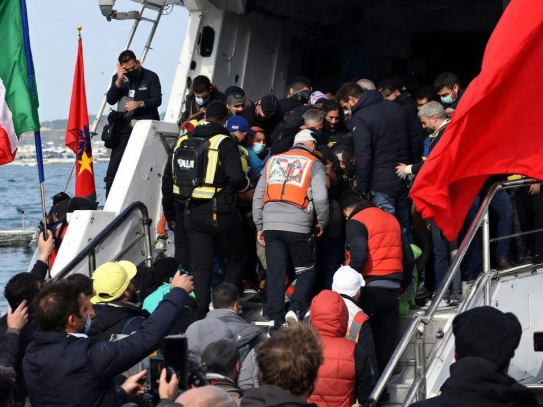 Migrants arriving at a port with flags in background.