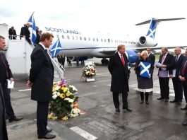 Plane on tarmac with officials and supporters present.