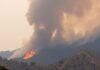 Smoke billows from hillsides as flames consume trees.