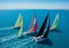 Sailboats racing across a blue ocean towards a distant coastline.